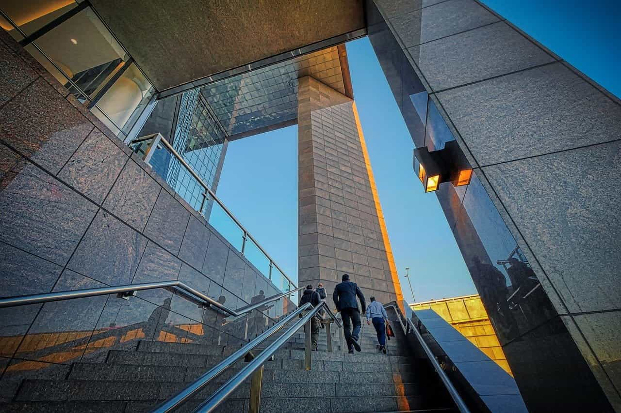 Mensen in formele kleding beklimmen de trappen van een bedrijfsgebouw.